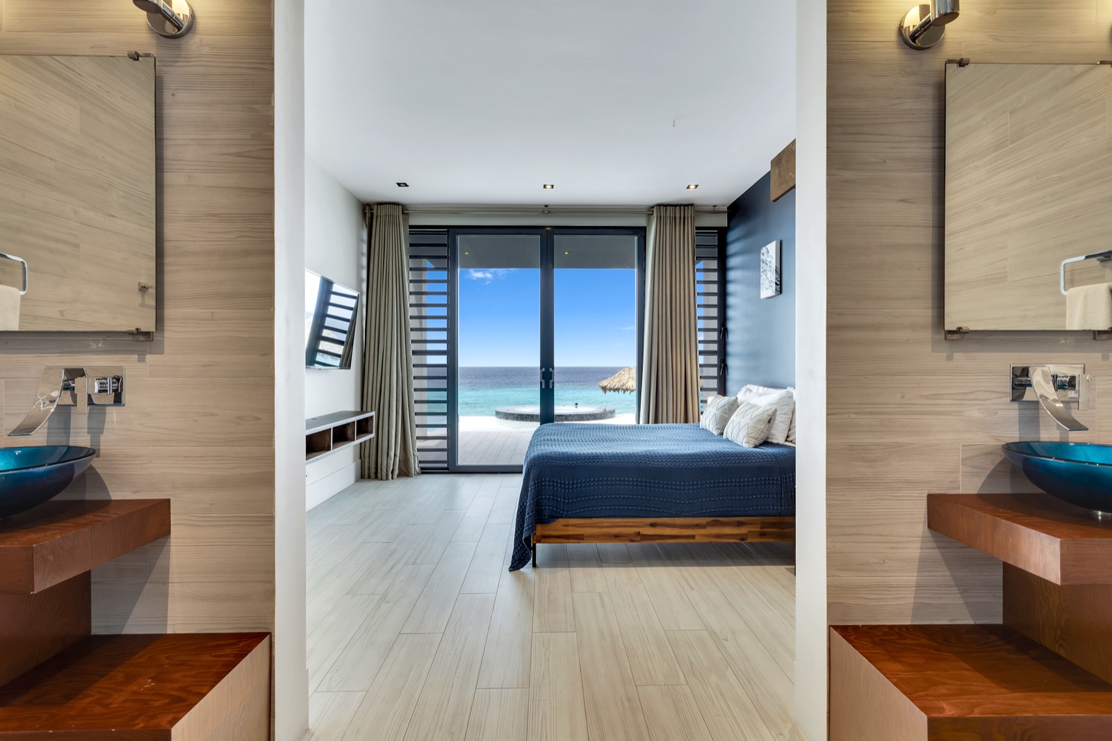 Luxury Bonaire villa master suite with king bed, en-suite double vanity, and panoramic ocean view through sliding glass doors to a private deck.
